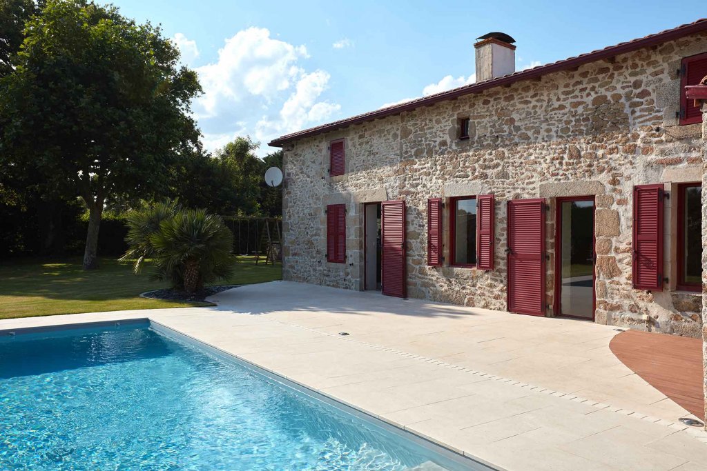 Longère rénovée avec terrasse en pierre calcaire Alhambra autour d’une piscine.