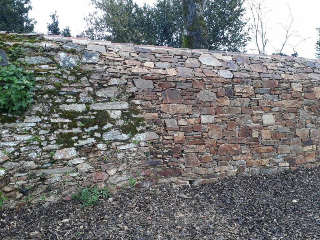 Mur ancien en pierre restauré avec des moellons de gneiss à Olonne-sur-Mer, partiellement recouvert de végétation sur la gauche.