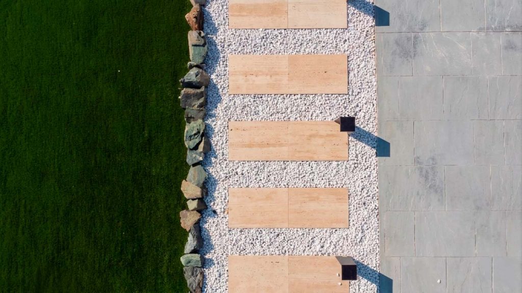 Une allée en travertin au design épuré, sublimée par le contraste entre la pierre naturelle, les galets blancs et les lignes contemporaines du jardin.