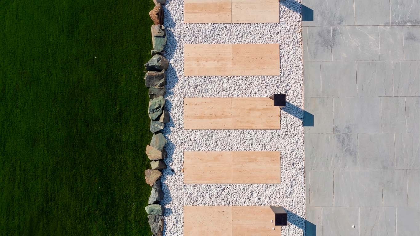 Une allée en travertin au design épuré, sublimée par le contraste entre la pierre naturelle, les galets blancs et les lignes contemporaines du jardin.